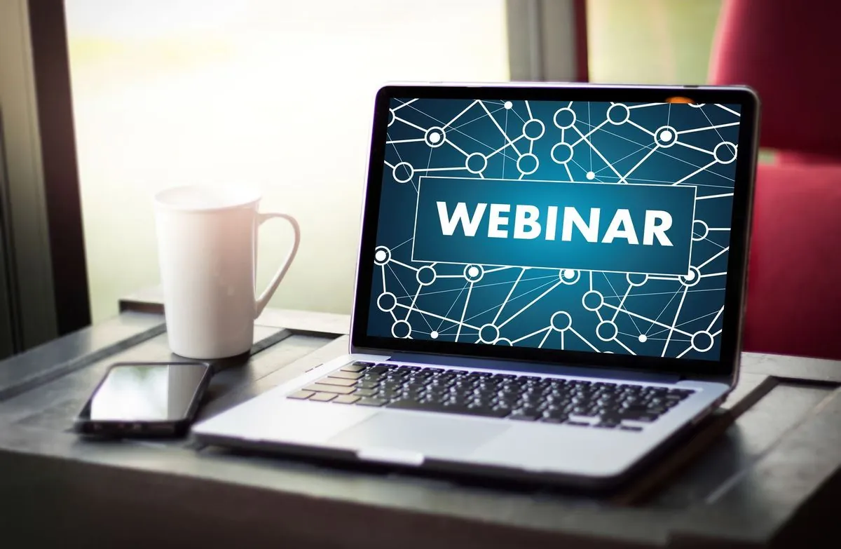 A laptop displaying the word webinar next to a cup of coffee